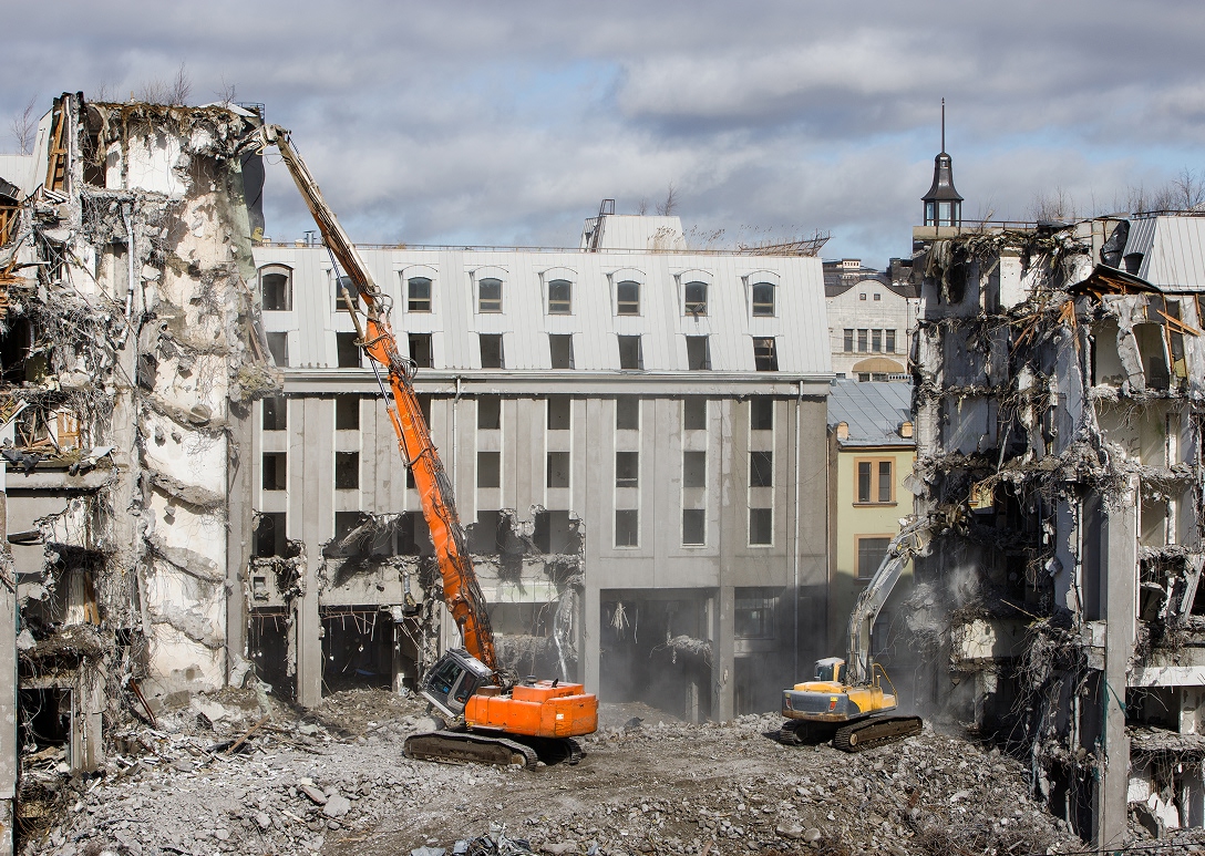 Excavadora con pinza demoledora derribando un edificio de concreto con riego para control de polvo